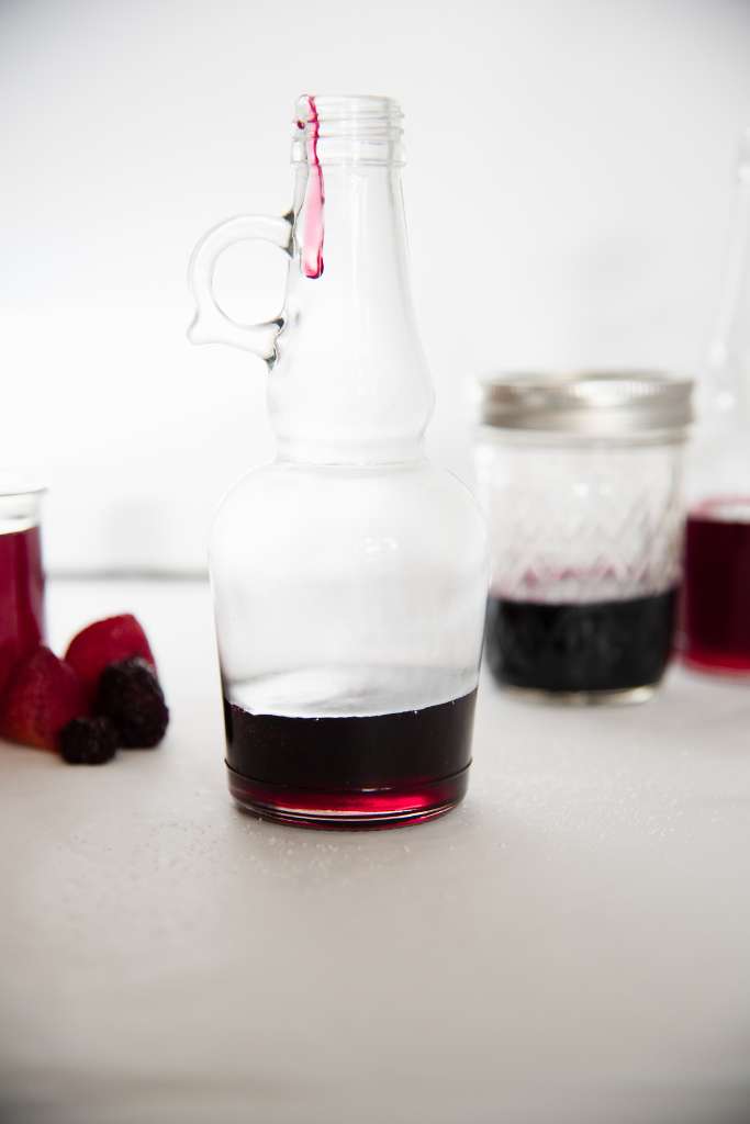 a glass bottle with berry simple syrup, there is a drop of syrup running down the side of the bottle