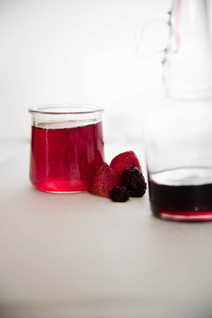 a little glass jar of syrup with strawberries and blackberries next to t