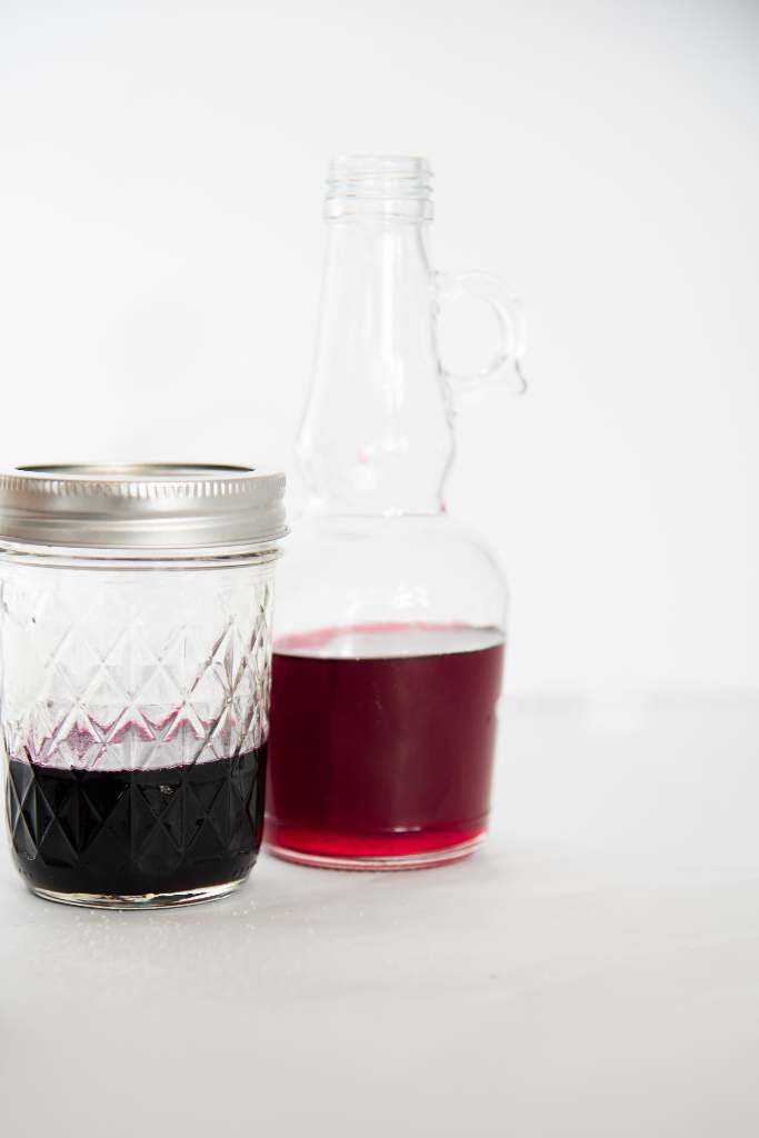 a jar with a lid and a glass bottle both full of berry syrup