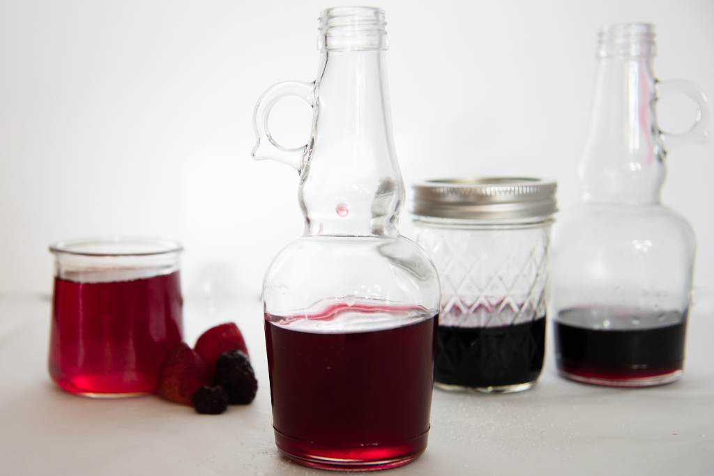 glass jars and bottles of berry simple, there are couple strawberries and blackberries next to one jar