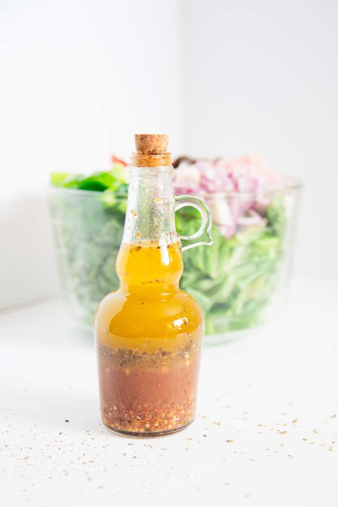 an unshaken bottle of greek salad dressing in front of a bowl of salad