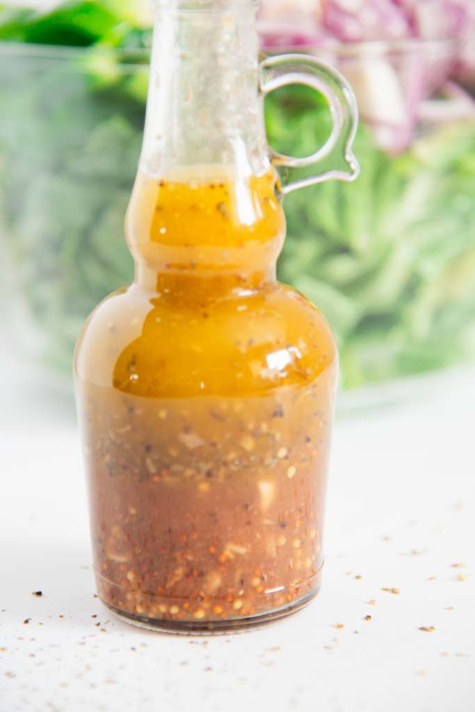 a bottle of salad dressing in front of a bowl of salad