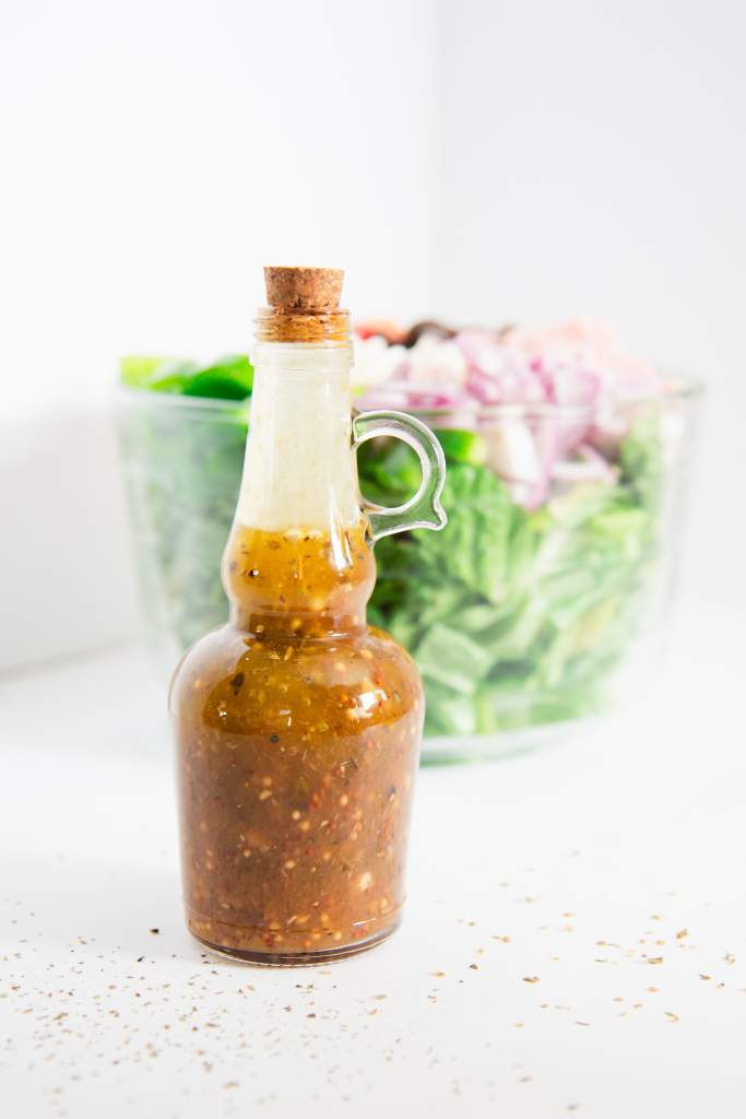 a bottle of Greek salad dressing in front of a bowl of salad 