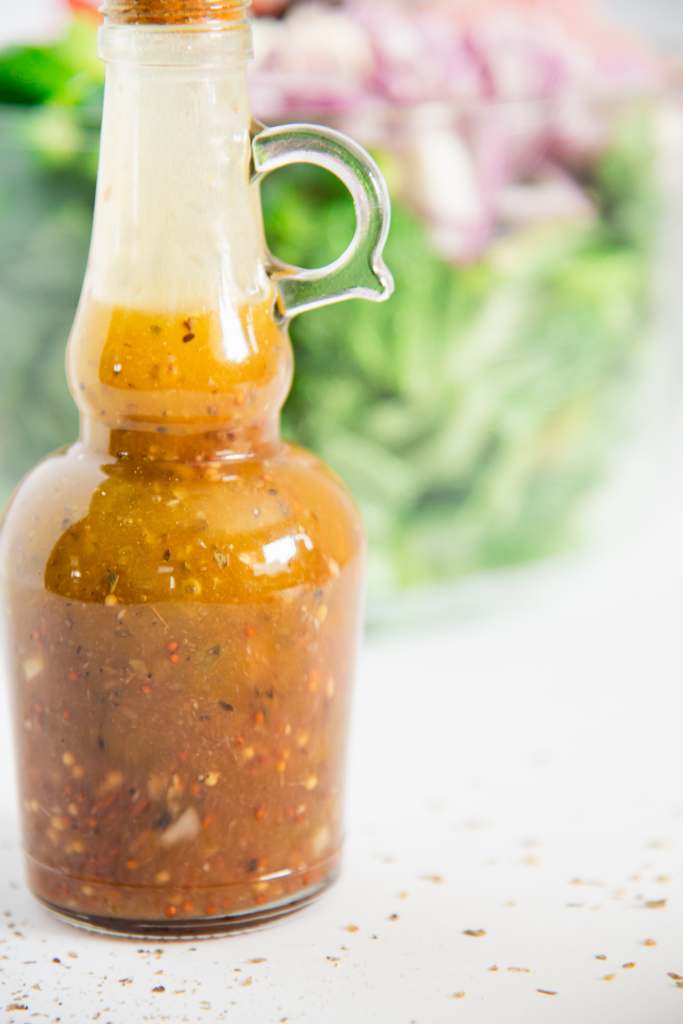 a close up of a bottle of salad dressing, the bottle is to the far left of the image and you can see bowl of salad behind it