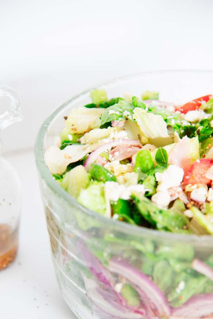 a cut of picture of a half of glass bowl of salad and part of bottle of salad dressing 