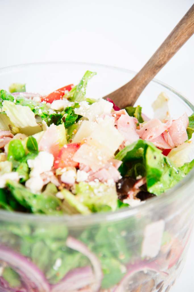 a close up of a finished salad with a wooden spoon in it 