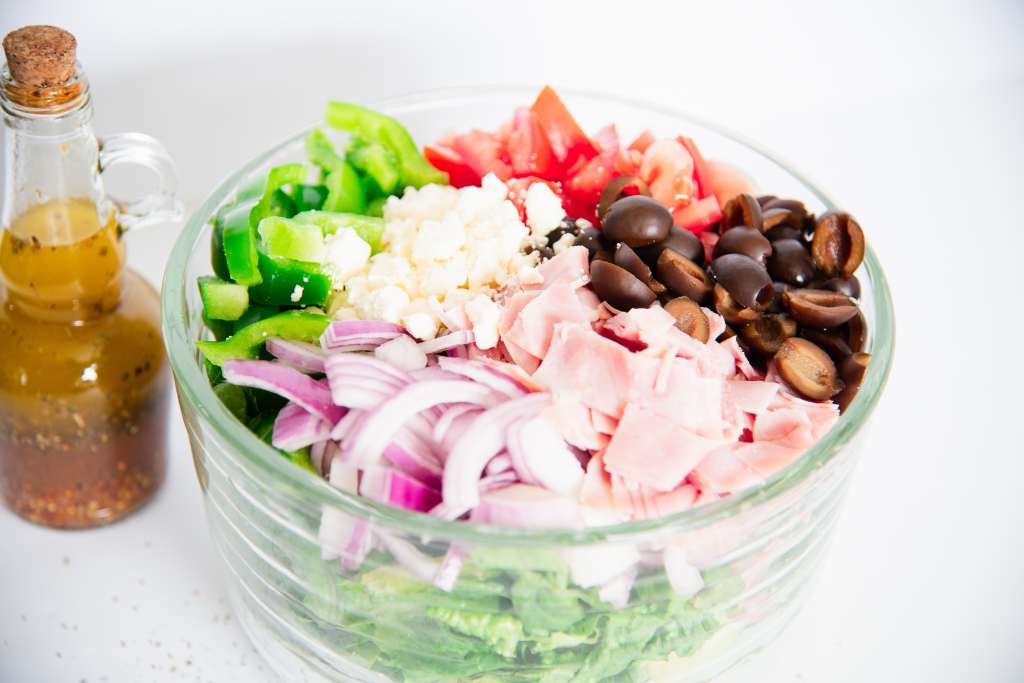 a bowl of lettuce with toppings on it not mixed in. And a bottle of salad dressing is sitting next to it