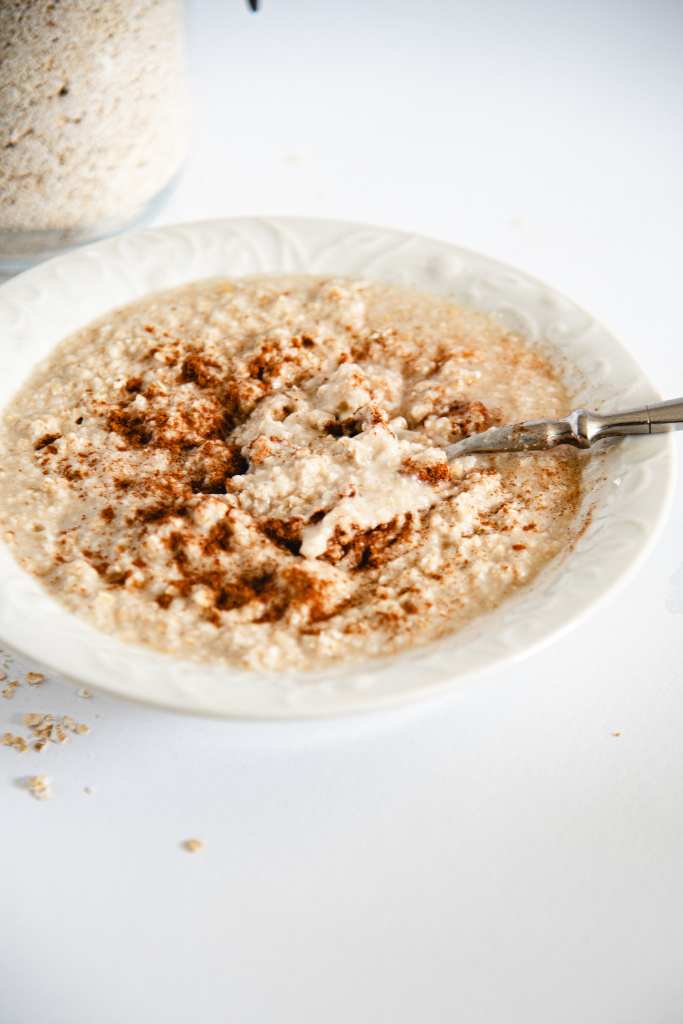 a close up of a stirred bowl of cooked oatmeal with a spoon in it and some cinnamon on it