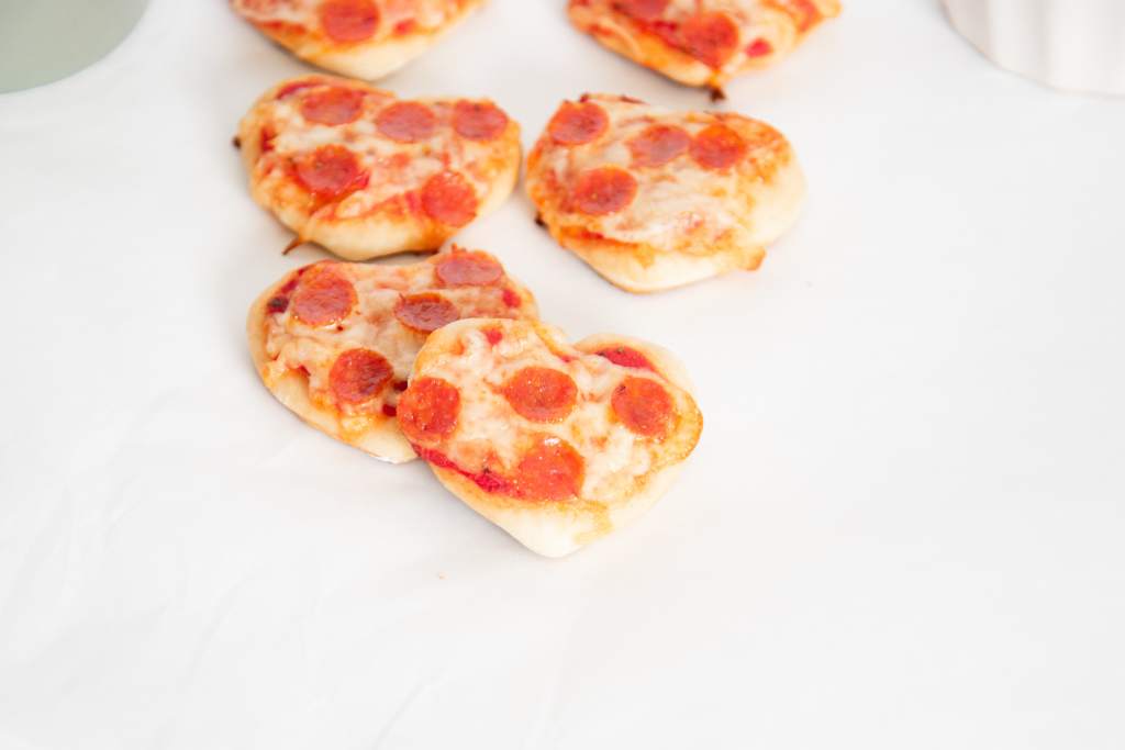 cooked mini heart shaped pizzas set out on a table, one is sitting on top of another one