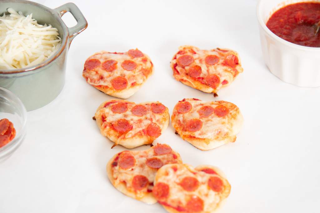 cooked heart shaped pizza, with topping toppings around them 