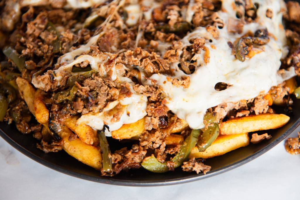 a close up of philly cheesesteak fries on a black plate