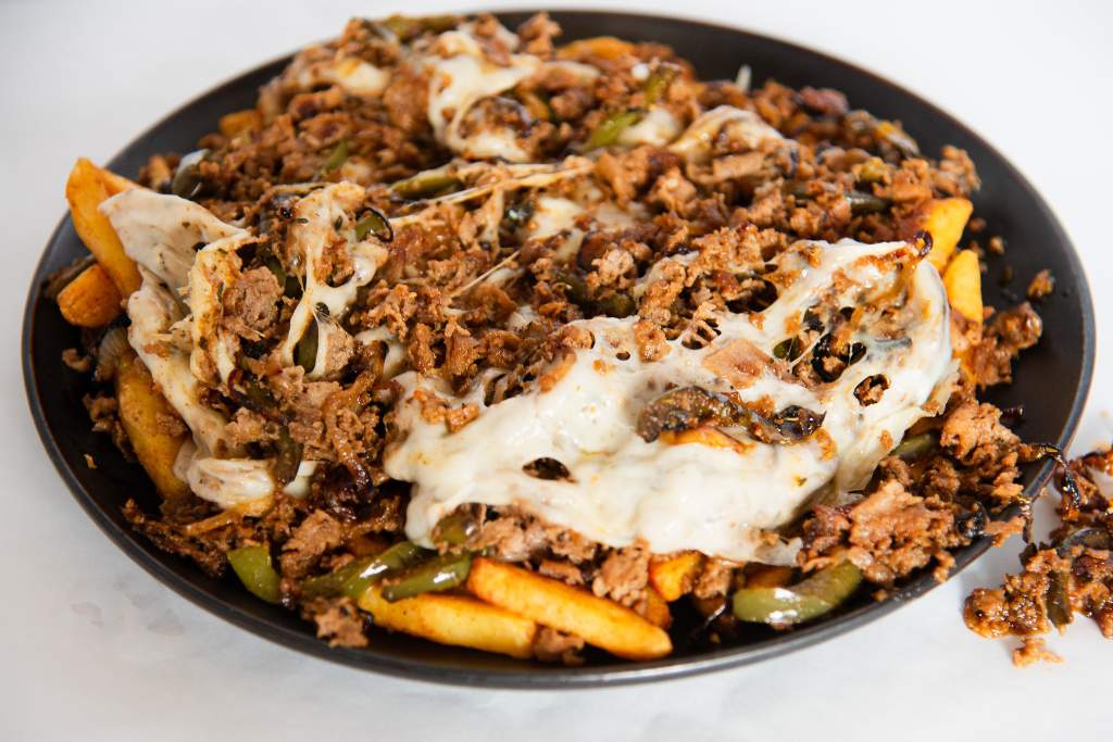 a plate of philly cheesesteak fries with some toppings spilled next to it