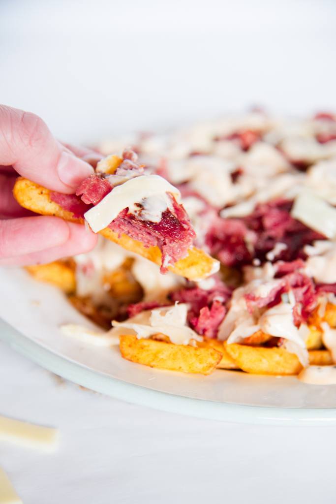 someone holding a couple french fires over a plate of fries