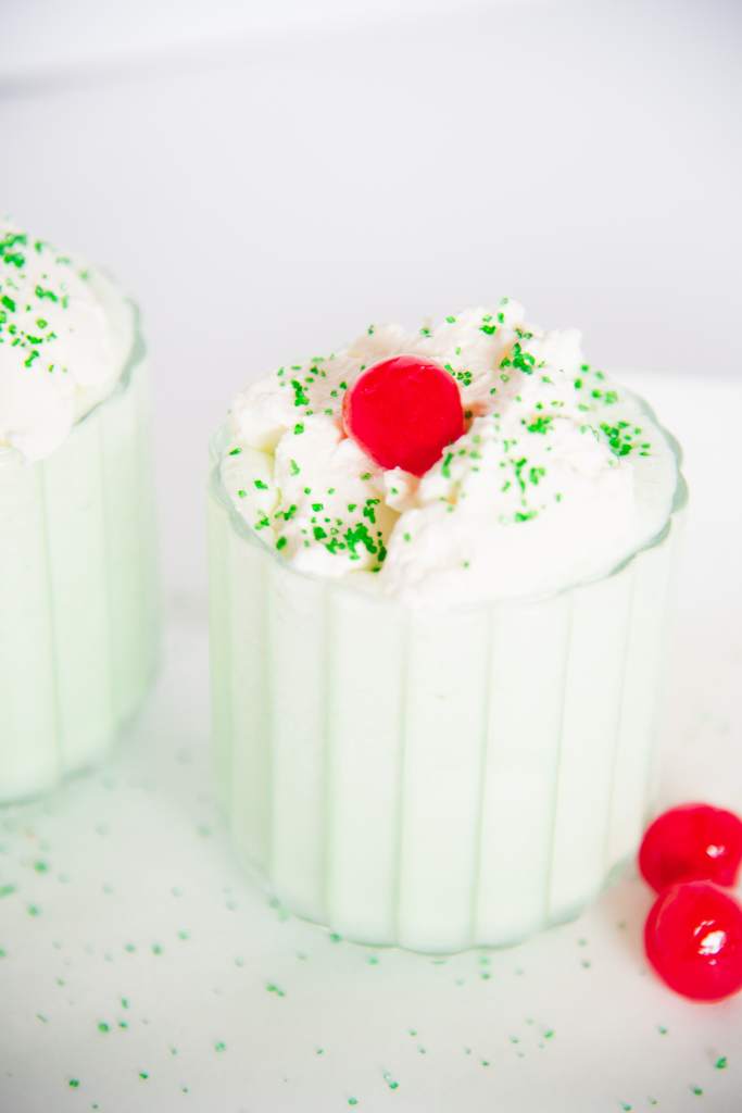 a finished shamrock shake with two cherries next to it, you can also see part of another shake next to it