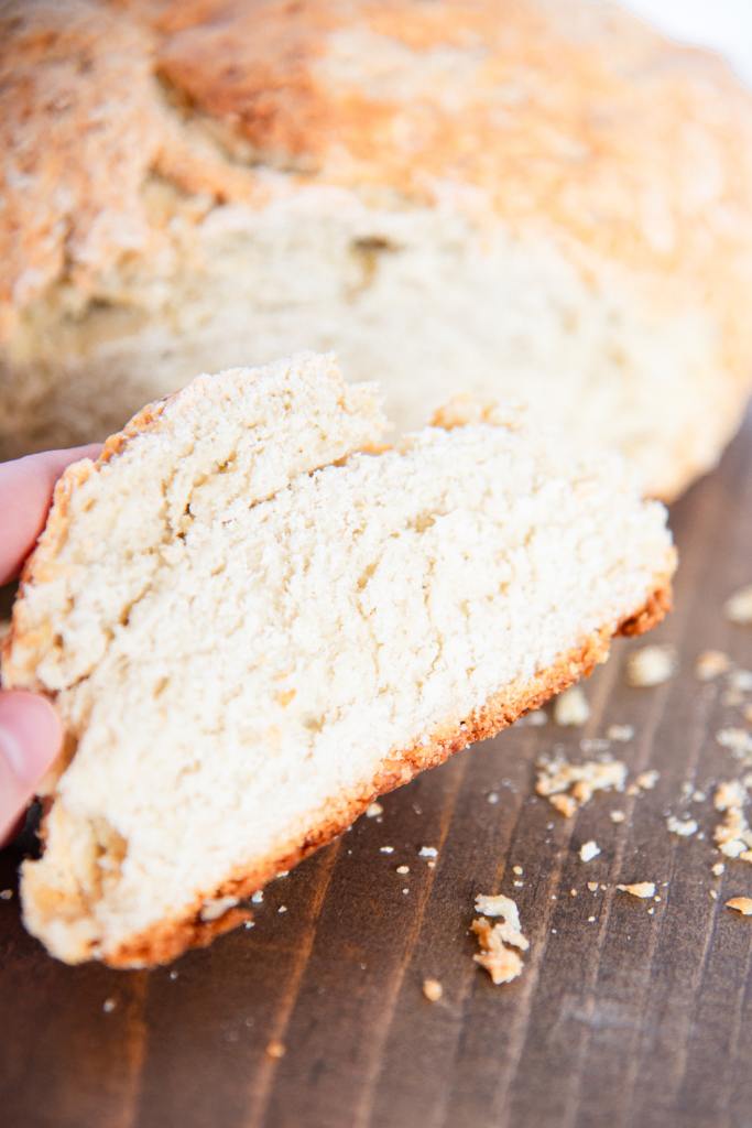 someone holding a slice of soda bread in front of the loaf