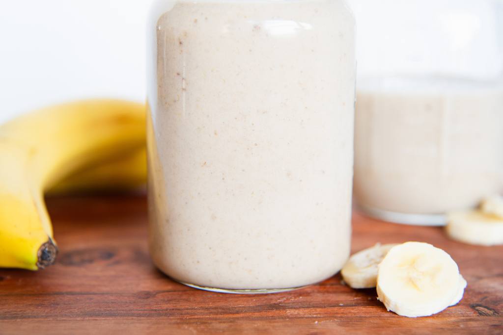 a close up of a poured banana shake with some banana slices next to it, and there is a whole banana next to it