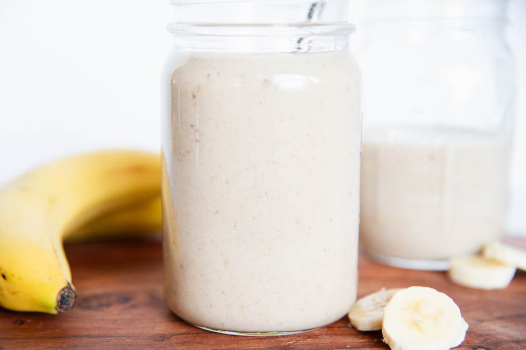 a banana shake in a mason jar, you can see another shake behind it, and some banana slices and a whole banana next to it 