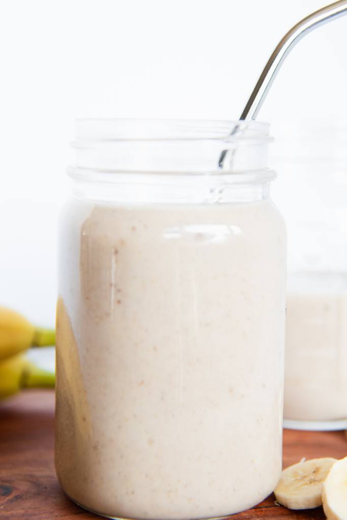 a banana shake in a mason jar with a metal straw in it, there is another jar behind it and some banana's next to it 