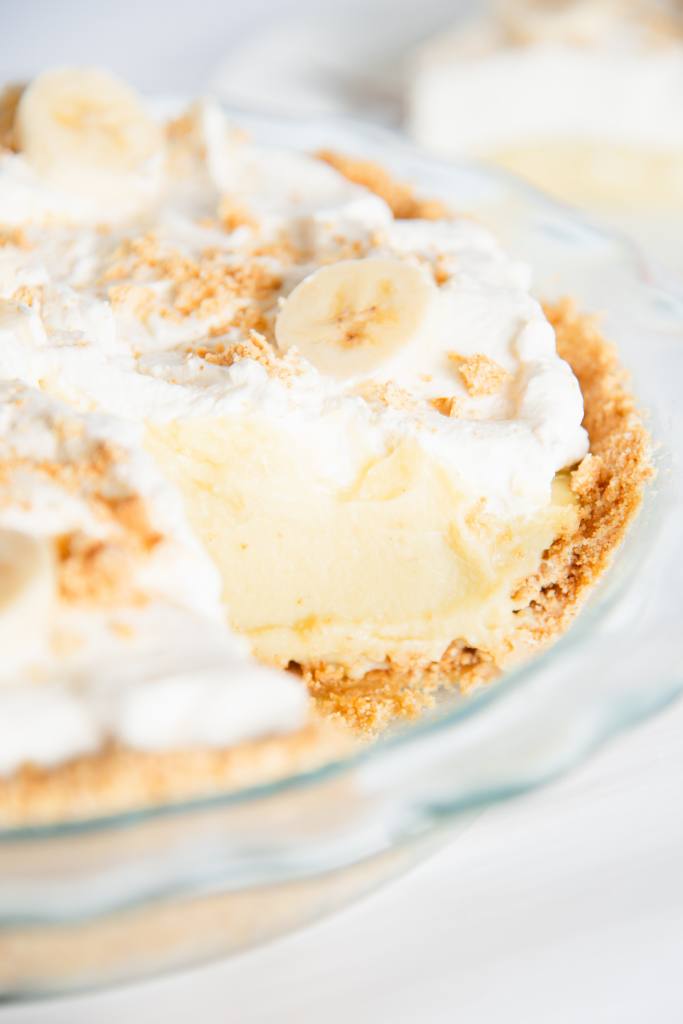 a banana cream pie with a slice taken out of it, you can faintly see a slice of pie on plate