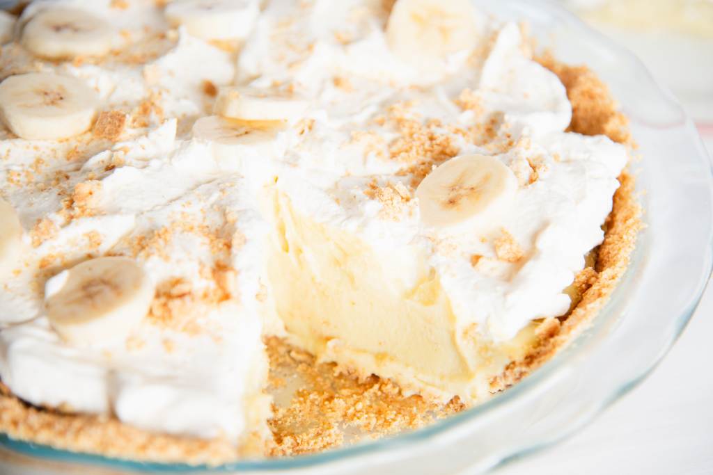 a banana cream pie in a glass pie dish with a slice taken out