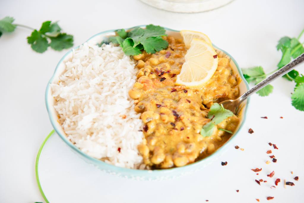 a bowl of rice and curried black-eyed peas with a fork in it and some melon slices and cilantro leaves on top