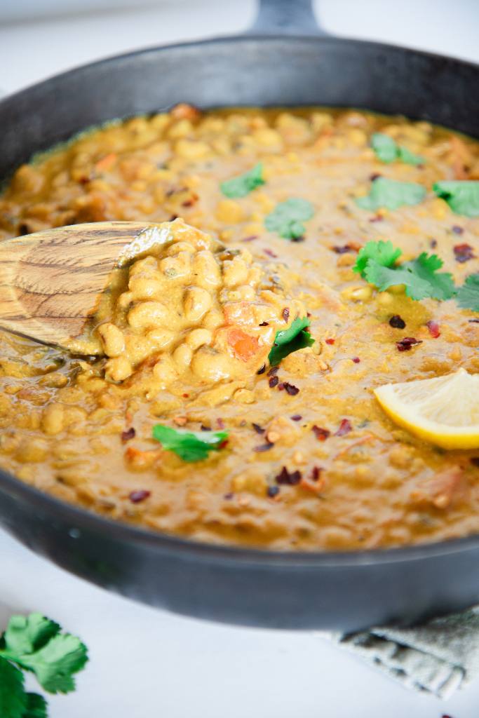 a close up of a wooden spoonful of curried black-eyed peas 