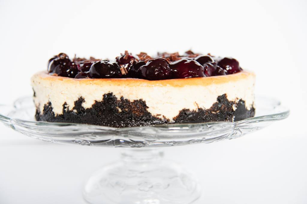 a side photo of a finished cheesecake on a glass cake stand 