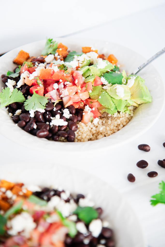 a quinoa bowl with a fork in it, there is another bowl near it and some black beans next to it 