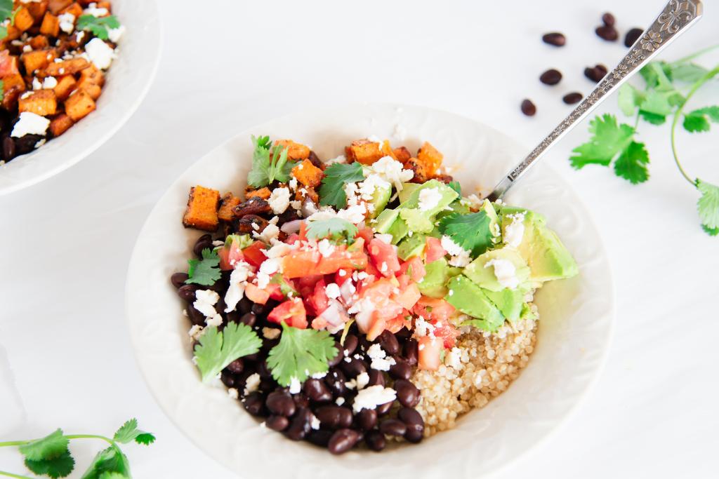 a quinoa bowl with a fork in it, there is another bowl off to the side and some cilantro and black beans around them