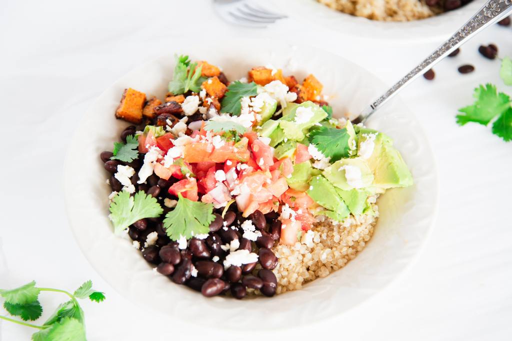 a quinoa bowl with a folk in it, there is come cilantro and black beans around it 