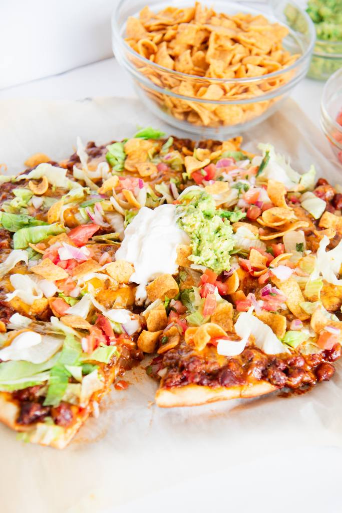 a finished and cut walking tacos pizza with a slice pulled slightly out from it. there are bowls with toppings next to it as well