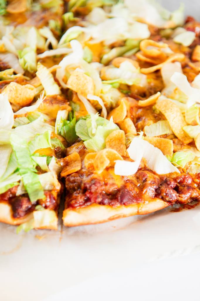 a cut pizza with just lettuce and chips on it 