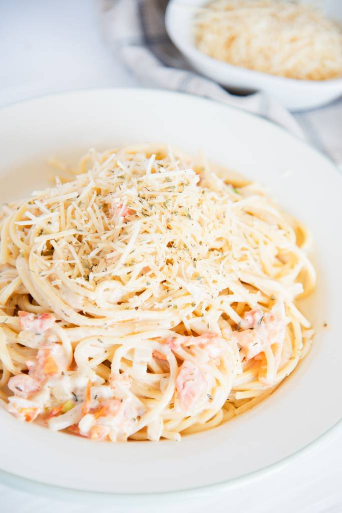 a plate of pasta with creamy white wine pasta sauce, there is a bowl of shredded cheese behind it 