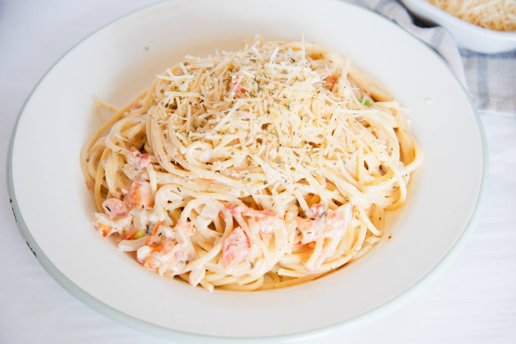 a plate of pasta with creamy white wine pasta sauce, there a bowl of shredded cheese next to the plate.