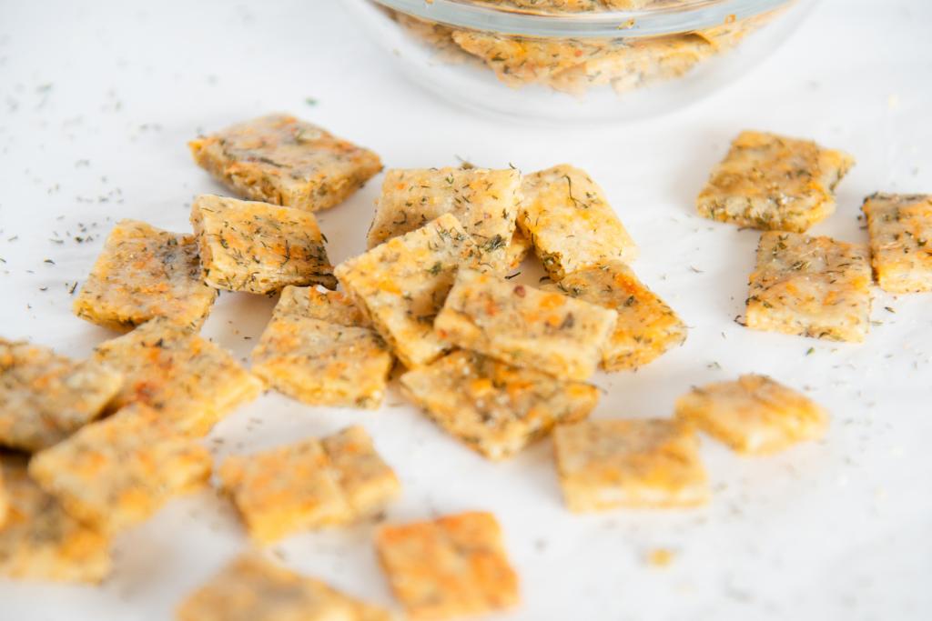 a close up of some crackers and dill weed, you can see a tiny part of the glass bowl of crackers behind them