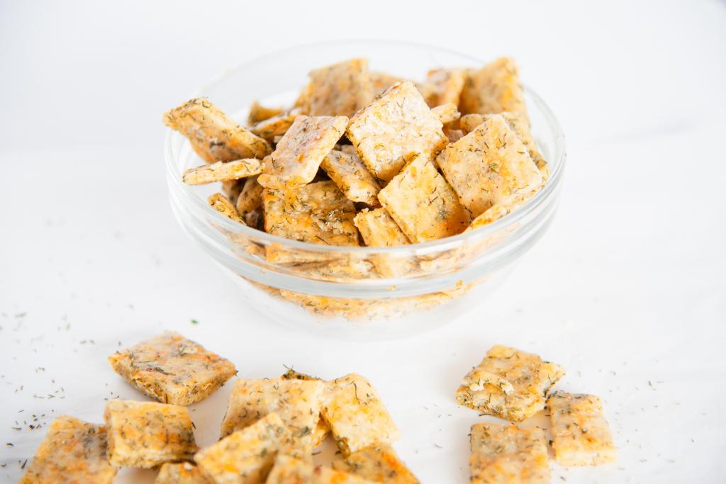 a small glass bowl of sourdough crackers, with some more crackers and some dill weed spilled in front of it