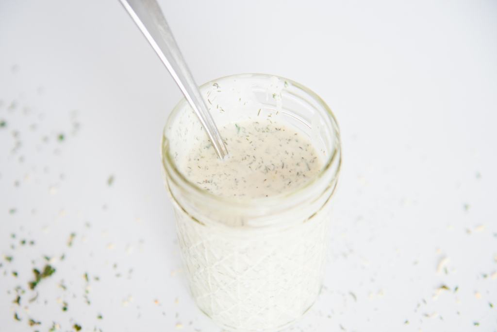 a jar of homemade ranch dressing with a spoon in it there is some dressing spilled on the edges