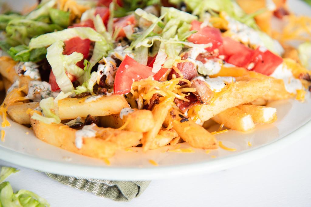 a close up on a plate of finished cheddar bacon loaded fries, there are a few pieces of lettuce next to the plate