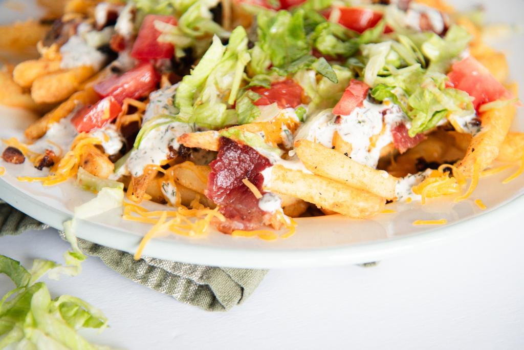 a plate of finished loaded fries, there is some shredded lettuce next to the plate