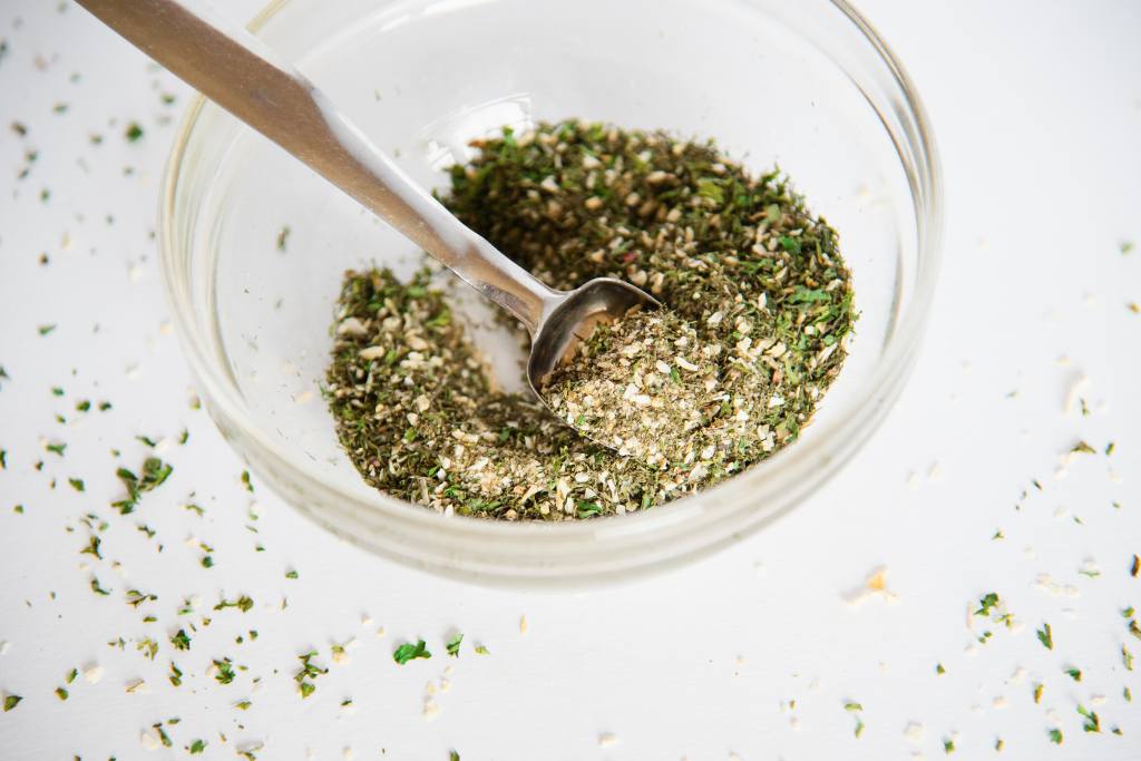 a glass bowl of spices with a metal measuring spoon in it