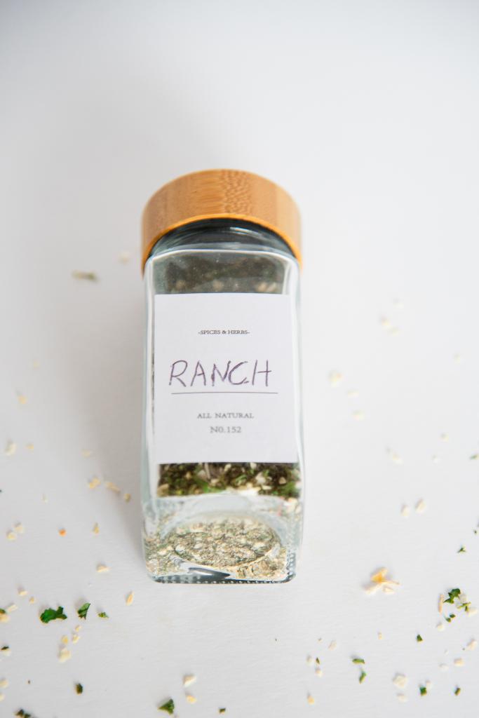 a glass spice bottle of ranch seasoning flaying on a table, it has a label that says ranch 