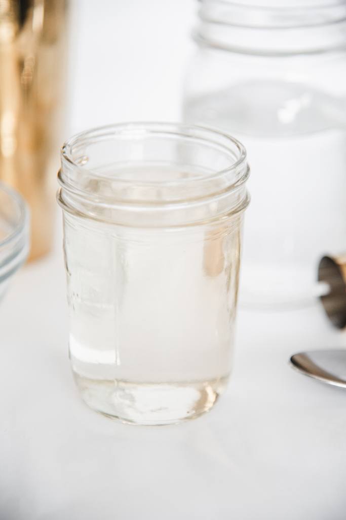 a jar of simple syrup with a jar of water, a small bowl, and cocktail shaking behind it