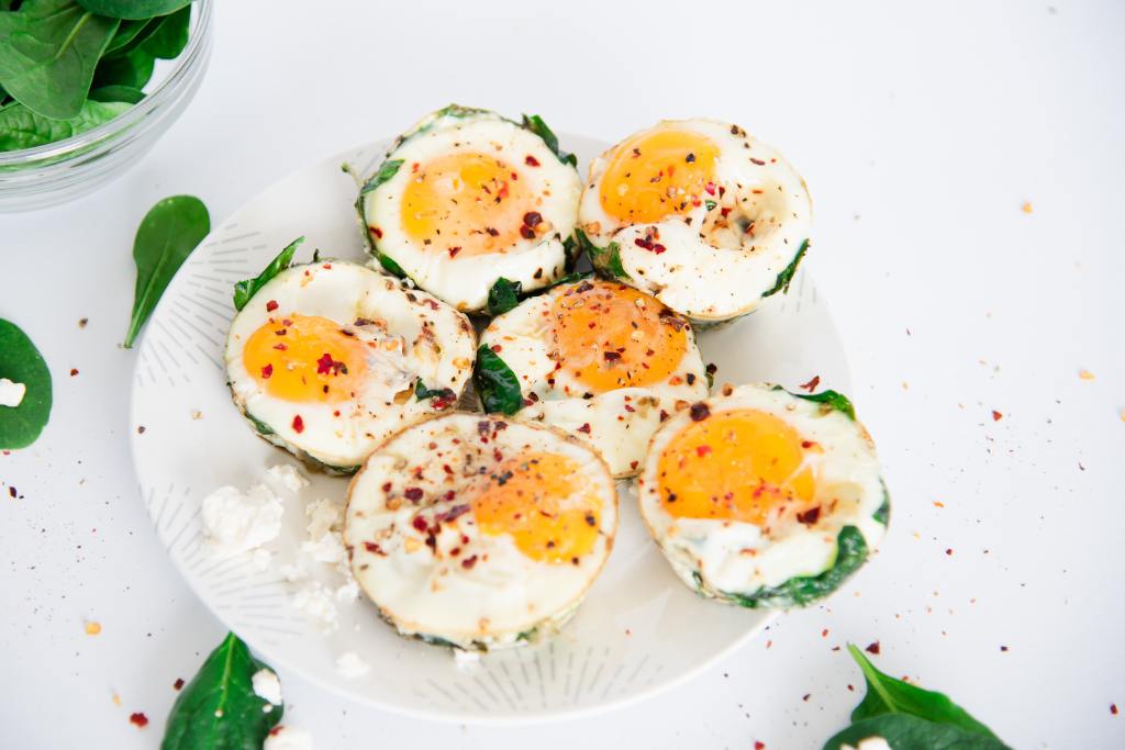 6 egg muffins on a plate with some feta cheese, there is a bowl of spinach to the left side of the plate