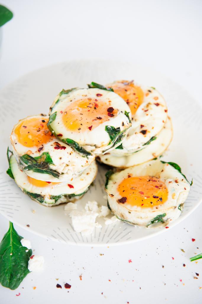 egg muffins stack on a plate with some feta cheese and spinach around it 