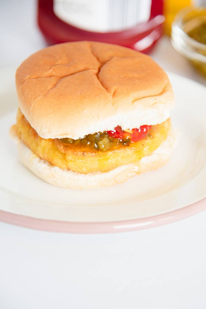 a veggie burger on a bun, there are some toppings in it, and some bottles behind the plate