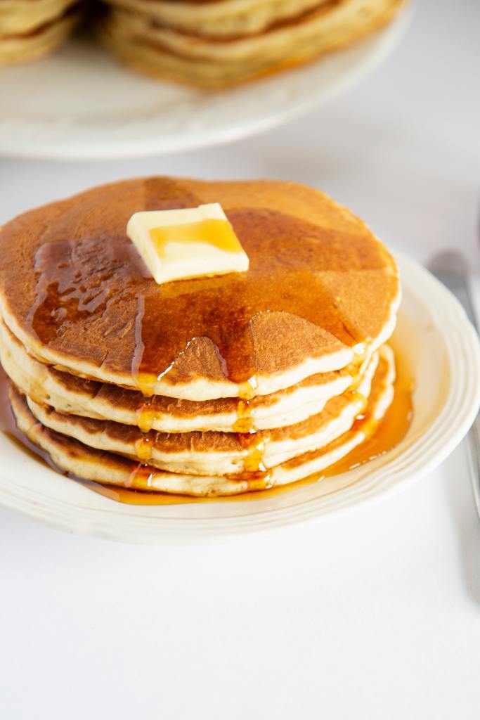 a close up a stack of pancakes with butter on top, and syrup on top and dripping down the sides of the stack