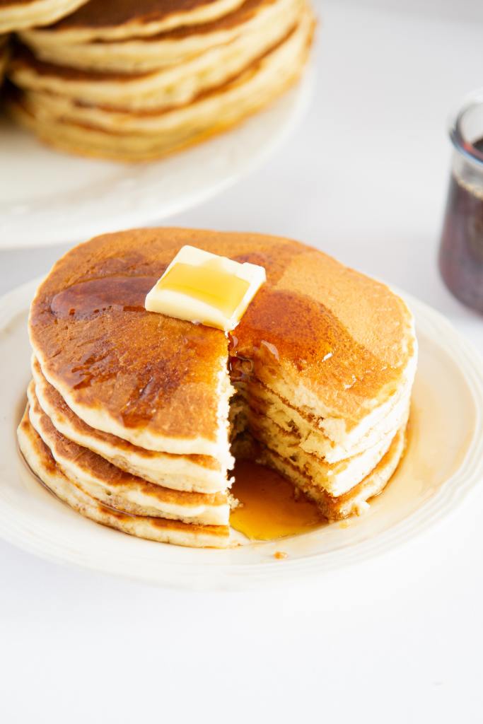 a stack of pancakes on a plate with section of them cut out, there is butter and syrup on top of them