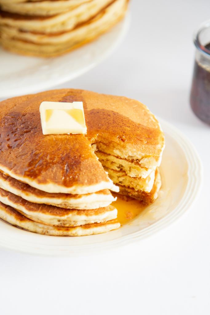 a close up of a stack of pancakes with a section cut out, there is butter and syrup on top