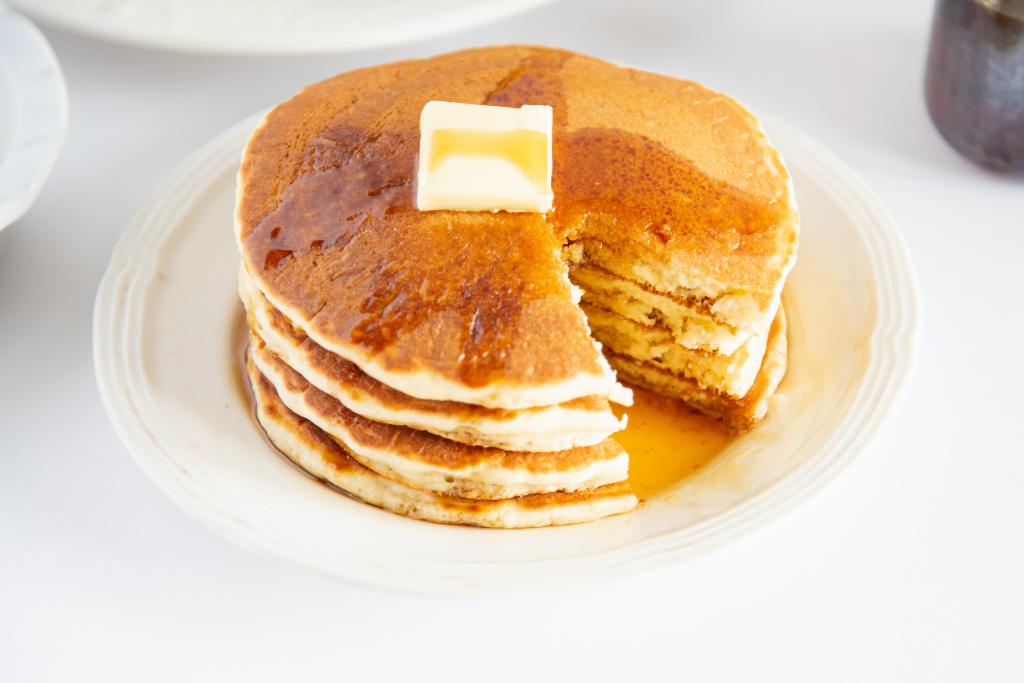 a close up of a stack of pancakes on a plate with butter and syrup on them, a section of the pancakes have been cut up