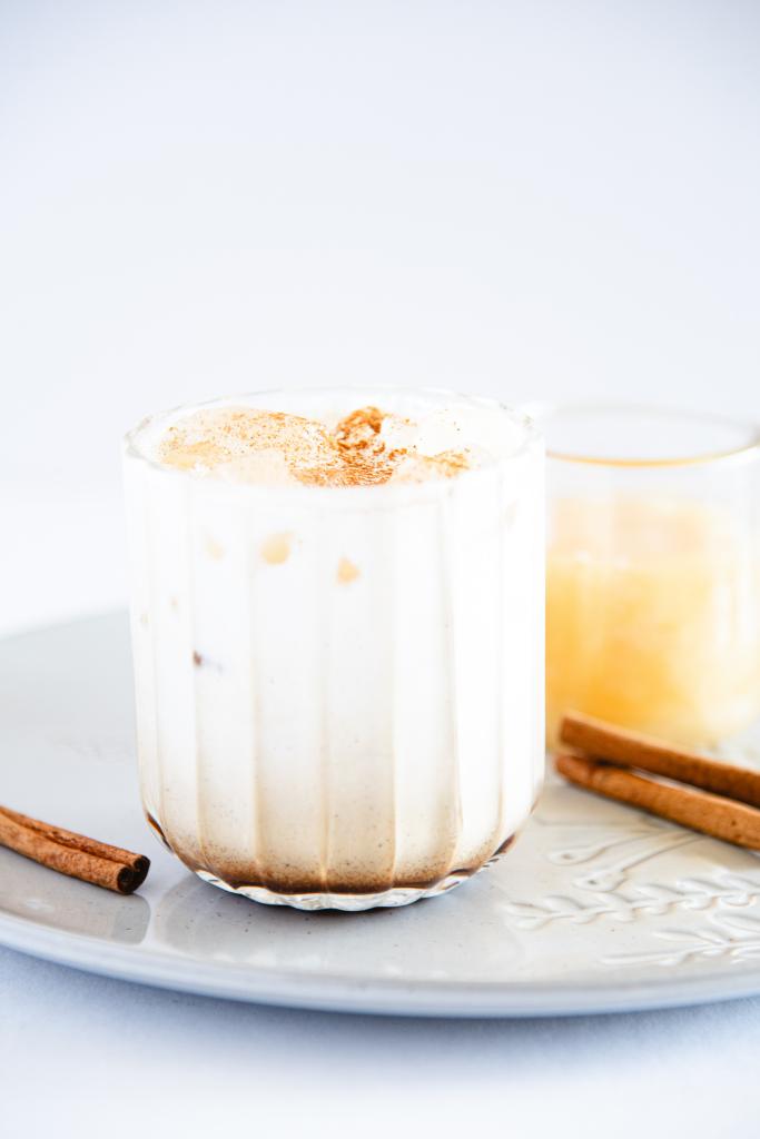 an iced honey cinnamon breve on a plate, there are some cinnamon sticks next to it and a jar of honey behind it